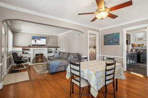 Dining room featuring arched walkways, ceiling fan, ornamental molding, a brick fireplace, and dark wood finished floors