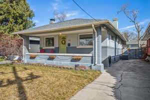 Bungalow with covered porch, a chimney, a front lawn, and brick siding