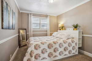 Bedroom with crown molding, dark carpet, and baseboards