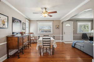 Dining room featuring arched walkways, dark wood-style flooring, and crown molding