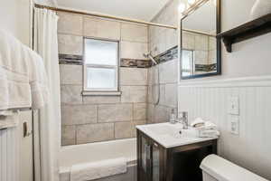 Bathroom featuring toilet, wainscoting, shower / bath combo with shower curtain, and vanity