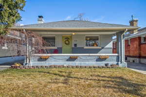 View of front facade with stucco siding, a front yard, a chimney, and brick siding