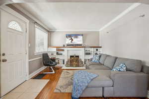 Living room with light wood finished floors, baseboards, crown molding, a textured ceiling, and a fireplace