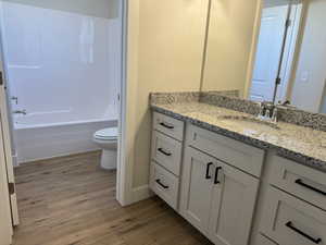 Bathroom with shower / tub combination, vanity, toilet, and wood finished floors