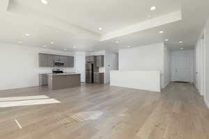 Unfurnished living room featuring light wood-style floors, a tray ceiling, baseboards, and recessed lighting