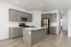 Kitchen with appliances with stainless steel finishes, light countertops, a sink, and gray cabinetry