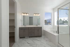 Bathroom featuring double vanity, marble finish floor, a garden tub, and a sink