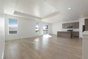 Unfurnished living room featuring light wood-type flooring, baseboards, a tray ceiling, and recessed lighting