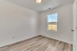 Spare room with light wood-style floors, visible vents, and baseboards