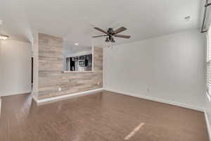 Unfurnished living room featuring wooden walls, baseboards, ceiling fan, an accent wall, and dark wood-style flooring