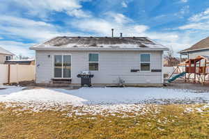 Snow covered house with entry steps, a lawn, fence, and a playground