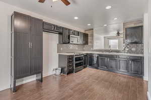 Kitchen featuring a sink, light countertops, appliances with stainless steel finishes, dark wood-style floors, and tasteful backsplash