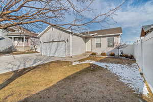 Back of house featuring fence, driveway, an attached garage, and a lawn