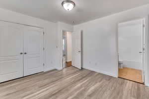 Unfurnished bedroom featuring ensuite bathroom, a closet, light wood-type flooring, and baseboards