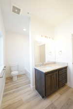 Bathroom featuring visible vents, toilet, vanity, wood finished floors, and baseboards