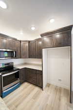 Kitchen featuring light stone countertops, light wood-style flooring, appliances with stainless steel finishes, and dark brown cabinets