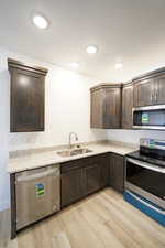 Kitchen with stainless steel appliances, a sink, dark brown cabinetry, and light wood-style floors