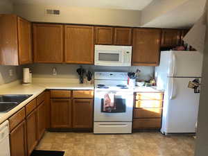 Kitchen featuring white appliances, a sink, visible vents, light countertops, and brown cabinetry