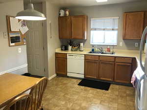 Kitchen featuring decorative light fixtures, light countertops, brown cabinetry, white dishwasher, and a sink