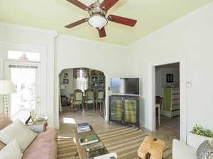 Living area featuring light tile patterned floors, ceiling fan, arched walkways, and ornamental molding