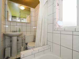 Full bathroom featuring shower / tub combo with curtain, tile walls, and toilet