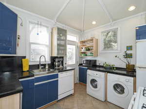 Kitchen with white appliances, blue cabinets, washing machine and dryer, open shelves, and a sink