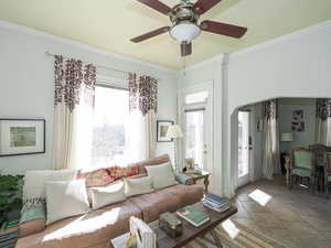 Tiled living room with ceiling fan, arched walkways, and crown molding