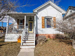 View of front of house with covered porch, a front lawn, and stucco siding