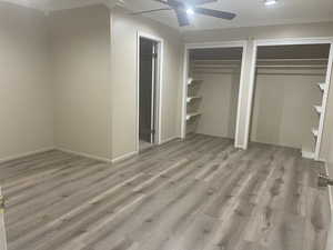 Unfurnished bedroom featuring ceiling fan, light wood-type flooring, crown molding, and two closets