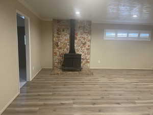 Unfurnished living room with hardwood / wood-style flooring, crown molding, a textured ceiling, and a wood stove