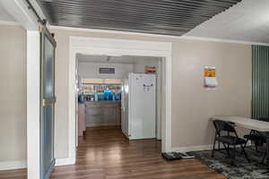 Hallway featuring baseboards, a barn door, dark wood-style flooring, and crown molding