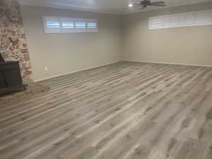 Basement featuring a wood stove, ceiling fan, light hardwood / wood-style floors, and crown molding