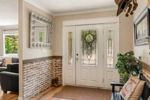 Entryway with ornamental molding, brick wall, and wood-type flooring