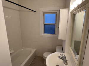 Bathroom featuring toilet, shower / tub combination, tile walls, and a sink