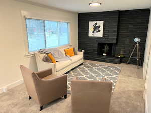 Carpeted living room featuring crown molding, a stone fireplace, and baseboards