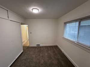 Unfurnished bedroom featuring baseboards, visible vents, dark colored carpet, and a textured ceiling