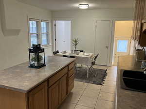 Kitchen featuring brown cabinets, a center island, a textured ceiling, a sink, and light tile patterned flooring