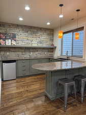 Bar with dark wood-type flooring, pendant lighting, a sink, and fridge