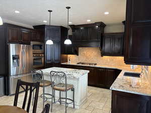 Kitchen with a sink, a center island, appliances with stainless steel finishes, decorative backsplash, and decorative light fixtures