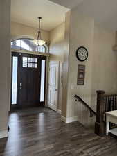 Entrance foyer with dark wood-style floors, a towering ceiling, and baseboards