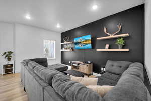 Living room with an accent wall, baseboards, wood finished floors, and recessed lighting