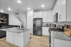 Kitchen with stainless steel appliances, an island with sink, a sink, and white cabinets