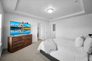 Bedroom with light carpet, visible vents, and a raised ceiling