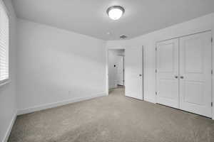 Unfurnished bedroom with a closet, light colored carpet, visible vents, and baseboards