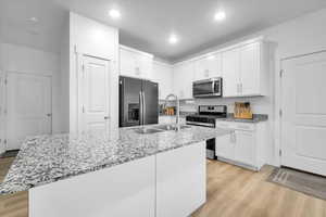 Kitchen with appliances with stainless steel finishes, light wood-type flooring, a kitchen island with sink, and white cabinets