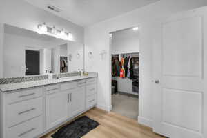 Full bath with wood finished floors, vanity, visible vents, baseboards, and a walk in closet