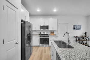 Kitchen with light stone counters, a sink, white cabinets, appliances with stainless steel finishes, and light wood finished floors