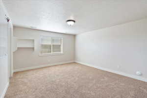 Empty room with light carpet, visible vents, baseboards, and a textured ceiling