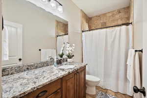 Bathroom featuring toilet, stone finish flooring, vanity, and a shower with curtain