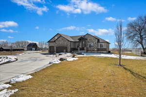 French country style house featuring an attached garage, fence, stone siding, driveway, and a front lawn